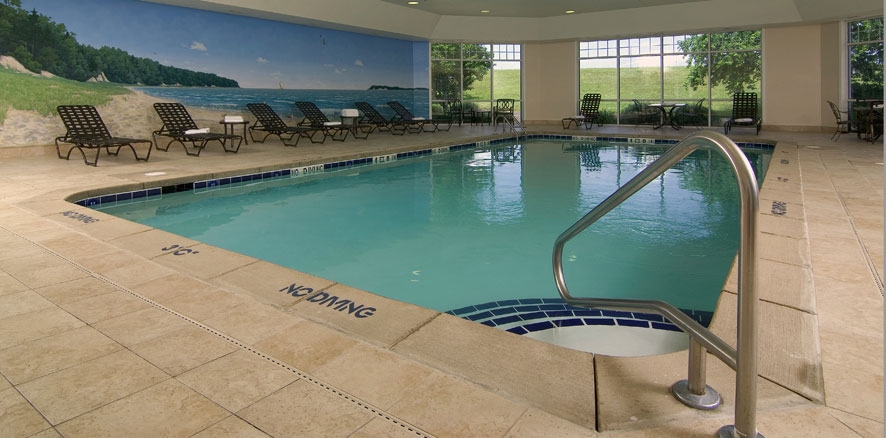 Piscine intérieure avec eau turquoise, fresque murale de plage, chaises longues et grandes fenêtres donnant sur la verdure