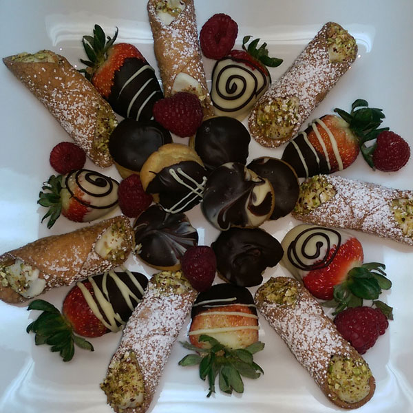 Plateau de viennoiseries, fraises enrobées de chocolat et cannoli disposés sur une assiette blanche