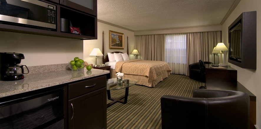 Chambre d'hôtel avec kitchenette équipée d'un micro-ondes et d'une cafetière, bol de pommes vertes, lit aux draps beiges